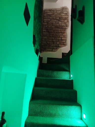 Stairs with green lighting leading up a corridor with textured walls.